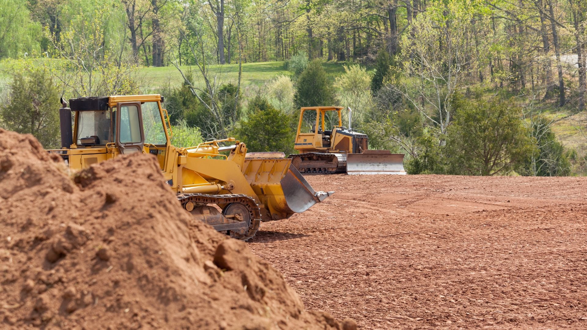 Yellow bulldozers clearing land in forest with dirt piles around